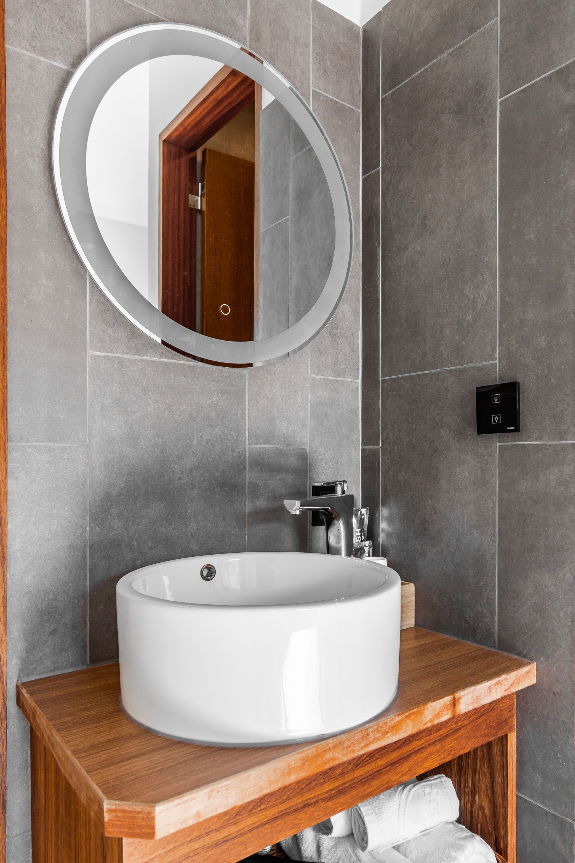 A modern bathroom with a large oval sink, wooden vanity, and a round mirror.