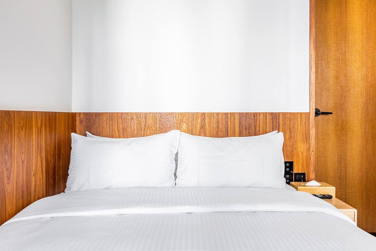 A neatly made bed with white linens, a wooden headboard, and a nightstand with a remote control and a tissue box.