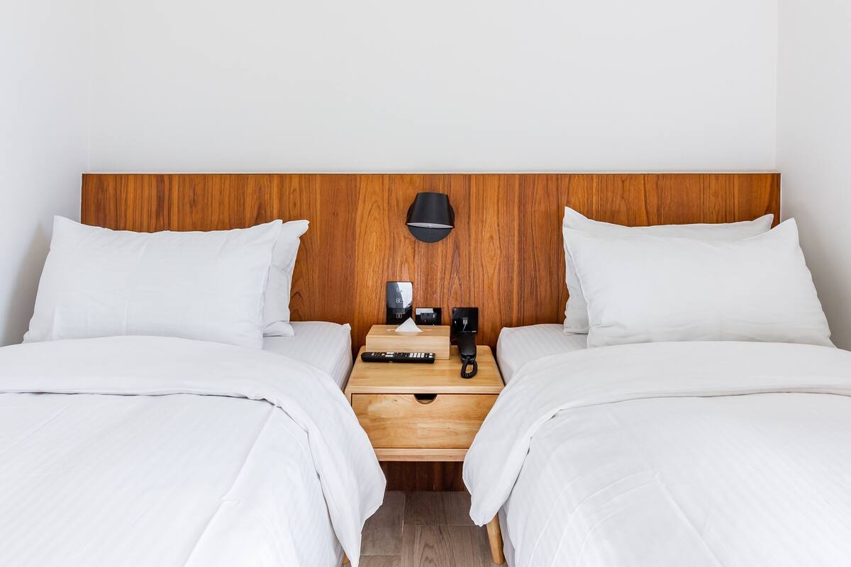 A double room with two beds, a wooden headboard, a bedside table with a lamp, a phone, and a remote control.