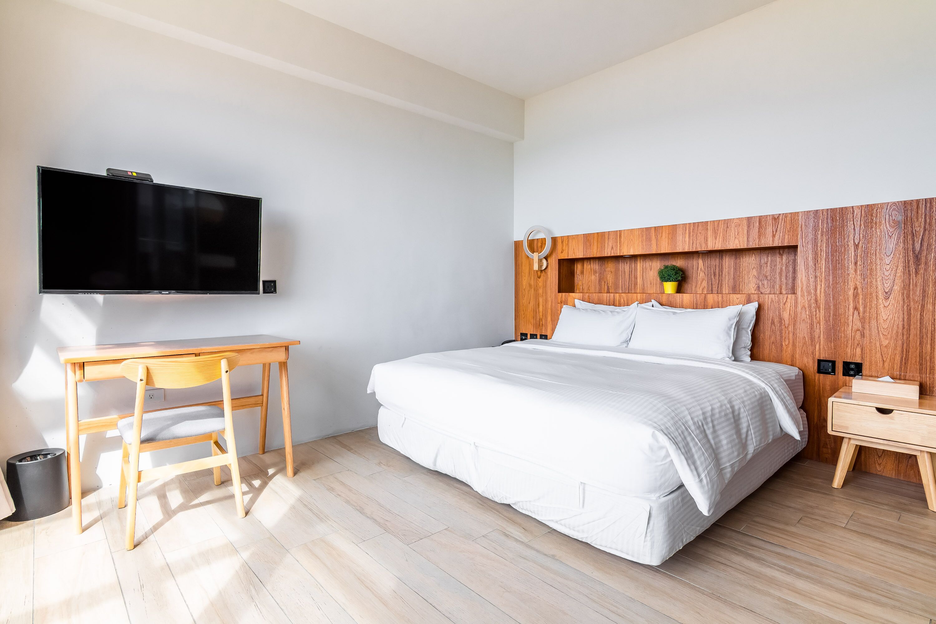 Une chambre à coucher moderne avec un lit, une tête de lit en bois, une table de chevet et un bureau avec une chaise.