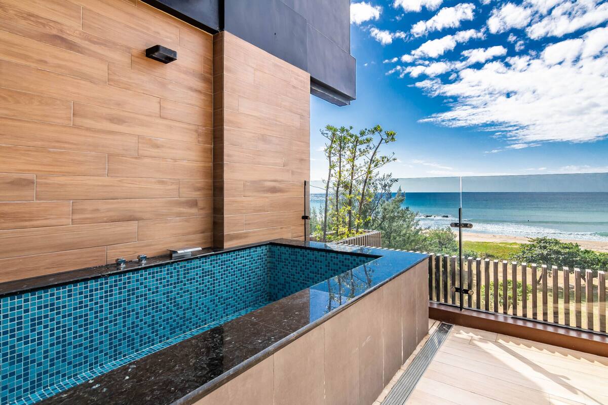 A modern outdoor pool with a wooden deck and a view of the ocean.