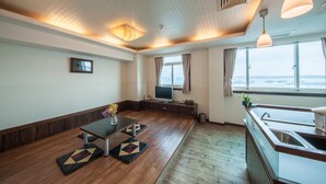 A modern living room with a wooden floor, a dining table, and a TV. There is a window with curtains and a view of the outside. - JiaHua Hotel (Magong)