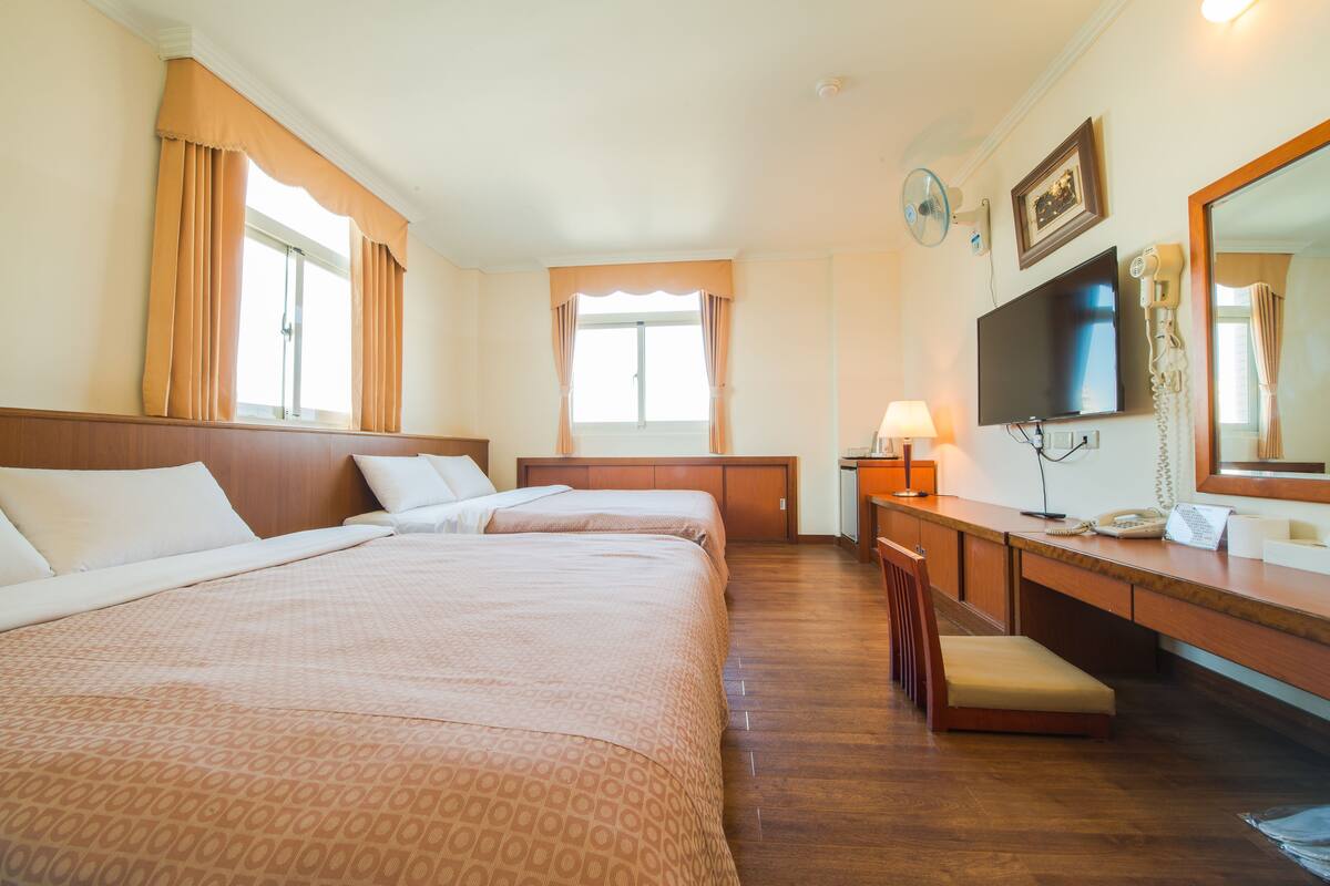 A hotel room with two beds, a desk with a lamp, a TV, a phone, and a mirror.