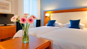 A hotel room with two beds, a TV, a vase with flowers, and a wooden table. - Hapimag Resort Athens (Athens)