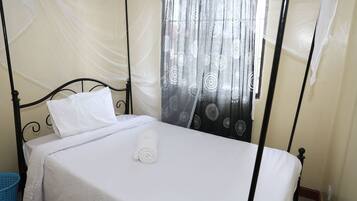 A bed with white linens, a rolled towel, and a mosquito net.