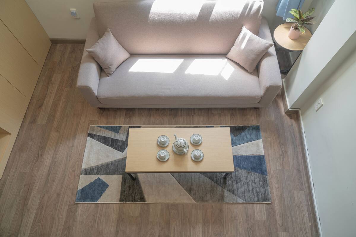 Un salon moderne avec un canapé beige, une table basse en bois sur laquelle sont posées des théières, et un tapis à motifs.