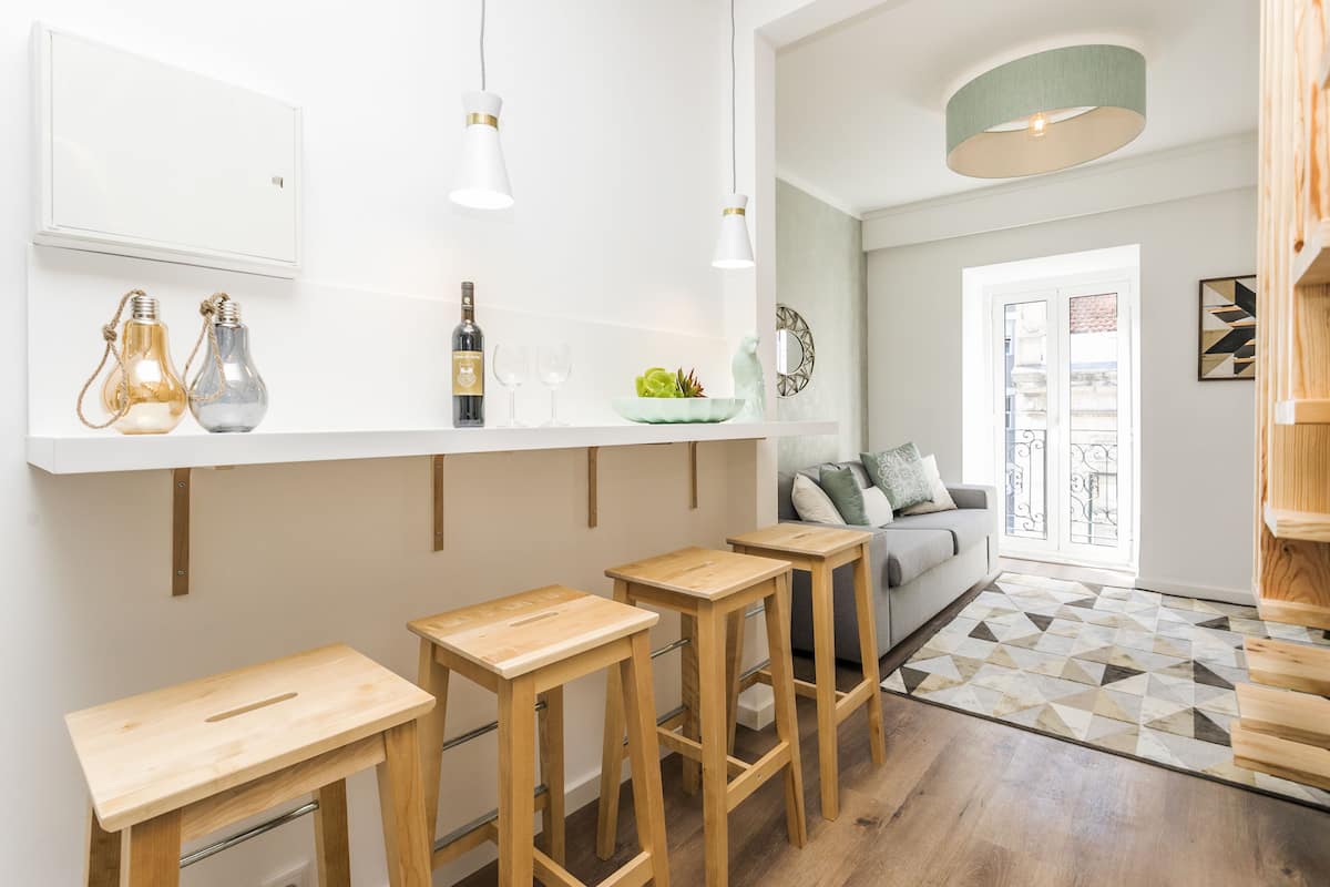 A modern kitchen with wooden stools, a white countertop, and pendant lighting.