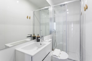 A modern bathroom with a large mirror, a white sink, and a glass-enclosed shower.