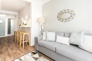 A modern living room with a grey sofa, wooden stools, a patterned rug, and a wall-mounted mirror.