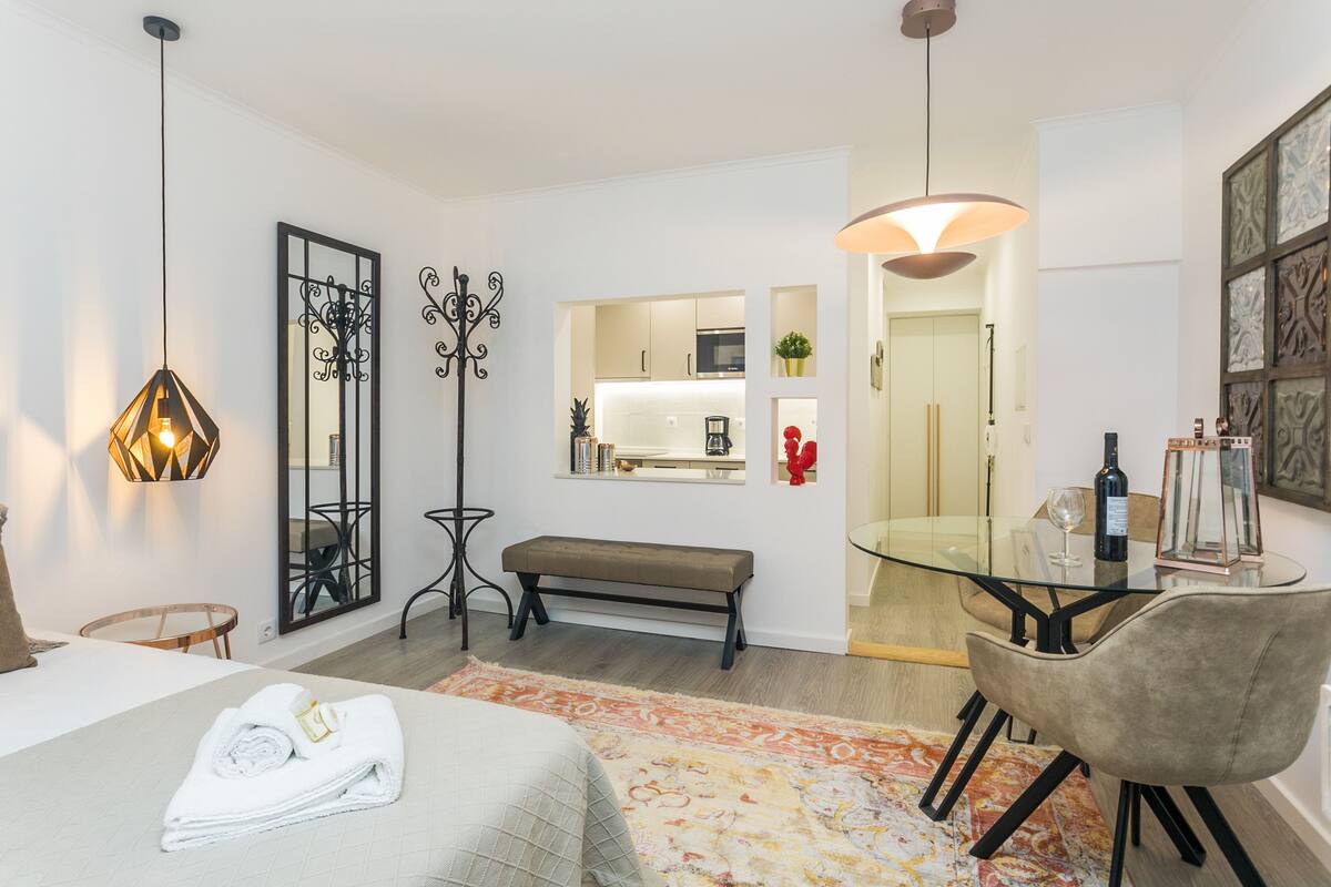 A modern hotel room with a glass dining table, a bench, and a bed with neatly folded towels.