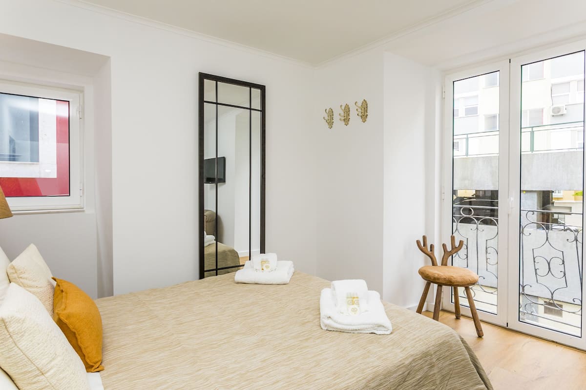 A hotel room with a bed, a chair, a mirror, and a sliding glass door to the outside.