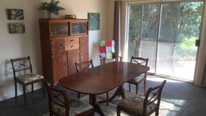 Un coin repas avec une table en bois et six chaises, un meuble avec des portes en verre, et une vue sur la verdure grâce à une porte-fenêtre coulissante.