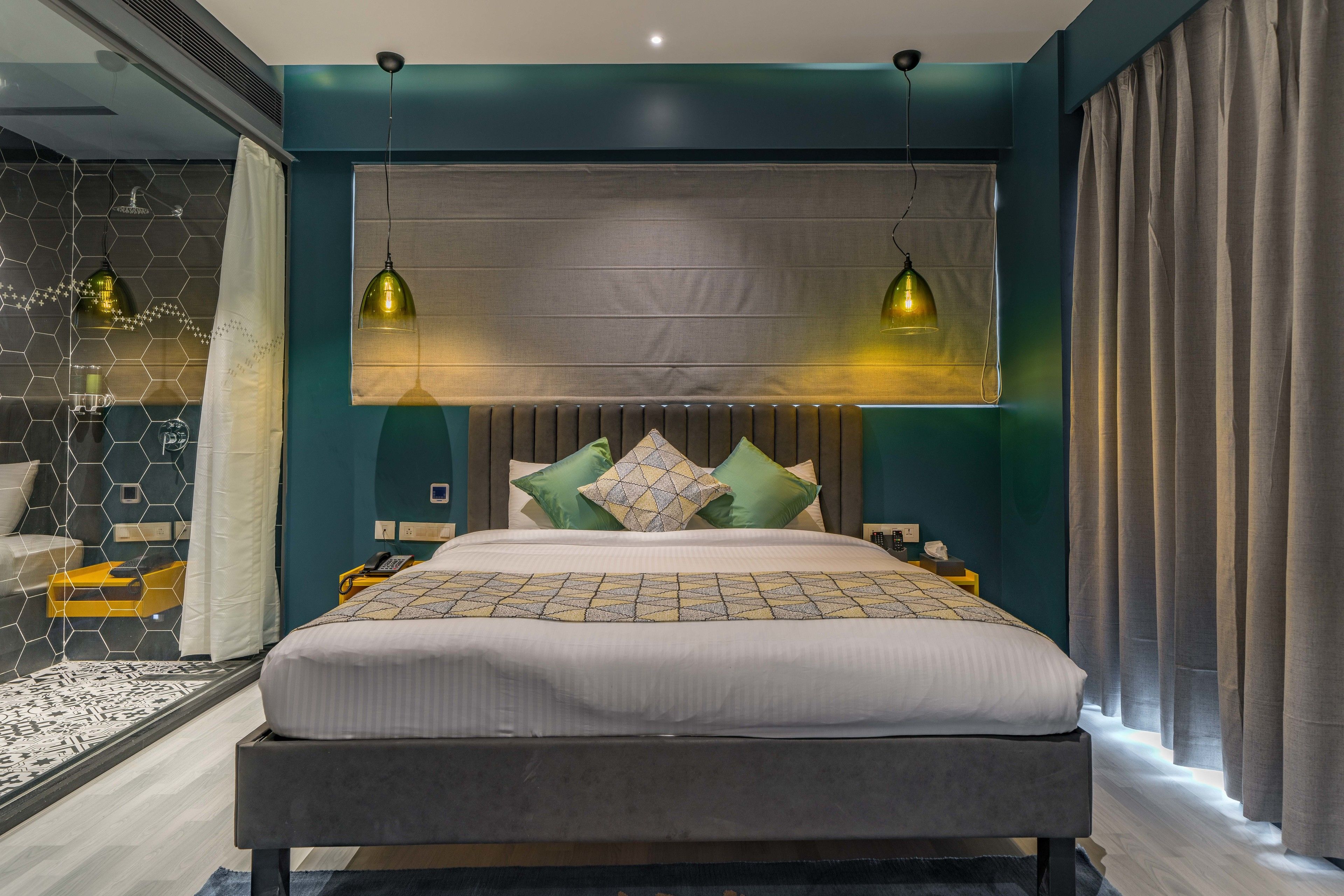A modern bedroom with a large bed, two pendant lights, a headboard, and a view of the bathroom.