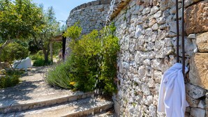 Mur de pedra amb una tovallola penjada d'una barra de metall, una escala de pedra i vegetació als voltants.