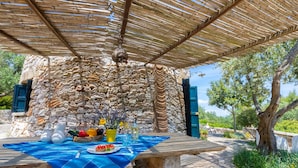Zona d'esmorzar a l'aire lliure amb mur de pedra de fons, taula preparada amb menjar i begudes, i estovell blau.