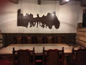 A restaurant interior with a long table and wooden chairs, a wall-mounted silhouette artwork, and a log wall on one side. - Lodge Hunter (Myoko)