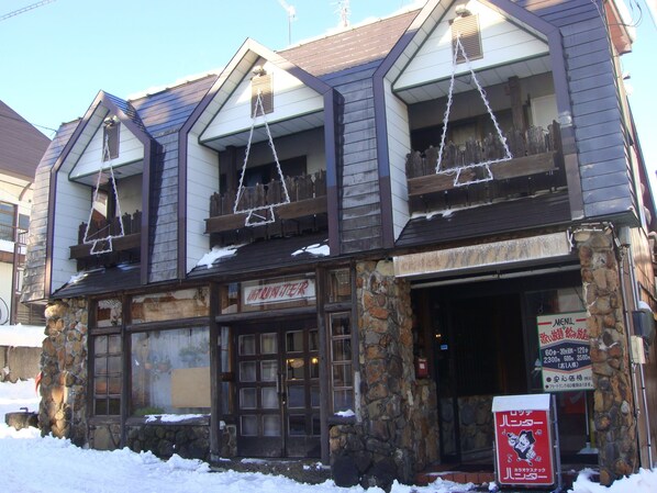 A stone building with a wooden facade, multiple windows, and a sign indicating a restaurant. - Lodge Hunter (Myoko)