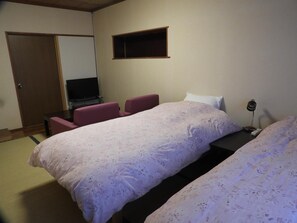 A hotel room with two beds, a television, a small shelf, and a desk with a lamp. - Lodge Hunter (Myoko)