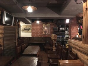 A rustic interior with wooden benches and tables, brick walls, and a vintage television. - Lodge Hunter (Myoko)