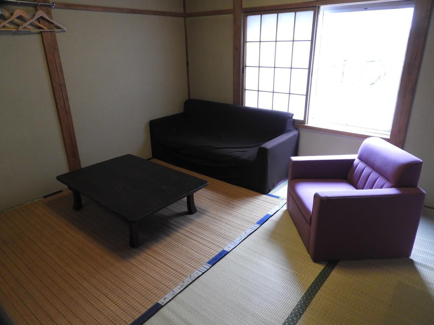 Una habitación con suelo de esteras de tatami, un sofá negro, una mesita y una silla morada.