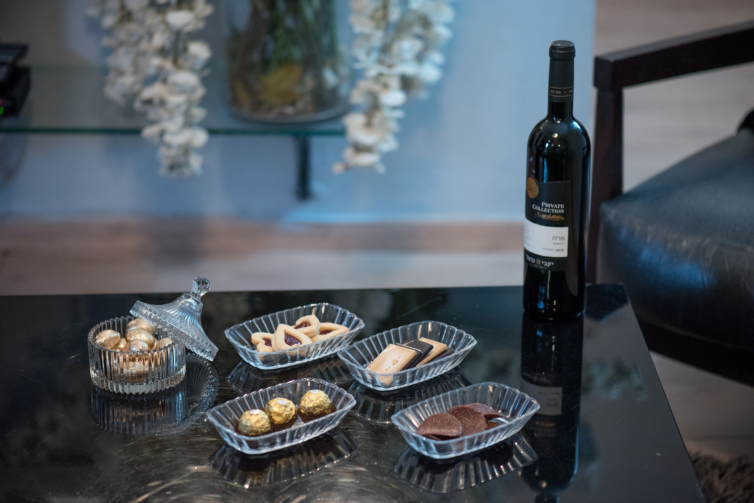 Una mesa de vidrio con cuatro recipientes de vidrio que contienen varios bombones y una botella de vino.