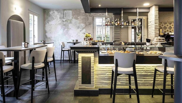 Een moderne bar met een wand van steen, barstoelen en diverse flessen op planken.