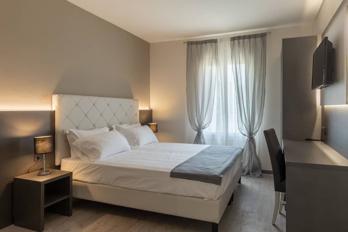 Moderni hotellihuone, jossa on suuri sänky, yöpöydällä olevat lamput, työpöytä ja televisio.