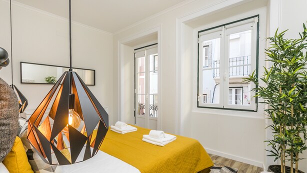 A hotel room with a bed, a hanging light fixture, a window with a view of buildings, and a potted plant. - LxWay Apartments Travessa da Peixeira (Lisbon)