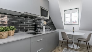 A modern kitchen with grey cabinets, a black tiled backsplash, a built-in microwave, and a coffee maker. There is a round table with two chairs and a bottle of wine on the right. - LxWay Apartments Travessa da Peixeira (Lisbon)