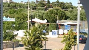 Un balcon avec une table dressée pour deux personnes, donnant sur un parking agrémenté d’un panneau indicateur et de quelques plantes.