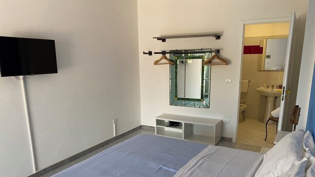 Une chambre d’hôtel avec un lit, un téléviseur fixé au mur, un miroir et une salle de bain visible à travers une porte ouverte.