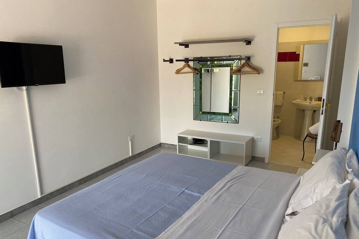 A hotel room with a bed, a TV mounted on the wall, a mirror, and a bathroom visible through an open door.