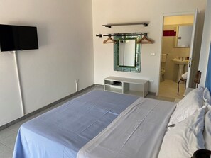 Habitación de hotel con una cama, un televisor montado en la pared, un espejo y un baño visible a través de una puerta abierta.