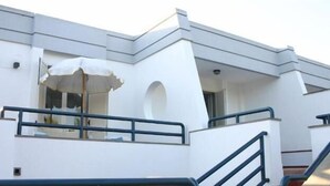 Un bâtiment moderne à la façade blanche, doté d’un balcon avec un parasol blanc et d’un escalier menant à un étage supérieur.