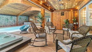 A cozy outdoor seating area with wicker furniture, a hot tub, and stone walls. - Panorama - Your Private Resort by Estes Park Homes (Estes Park)