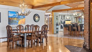 A dining area with a wooden table and chairs, a chandelier, and a painting of mountains. - Panorama - Your Private Resort by Estes Park Homes (Estes Park)