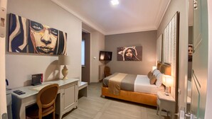 A hotel room with a bed, desk, chair, lamp, and artwork on the walls. - Halex Room & Food (Nettuno)