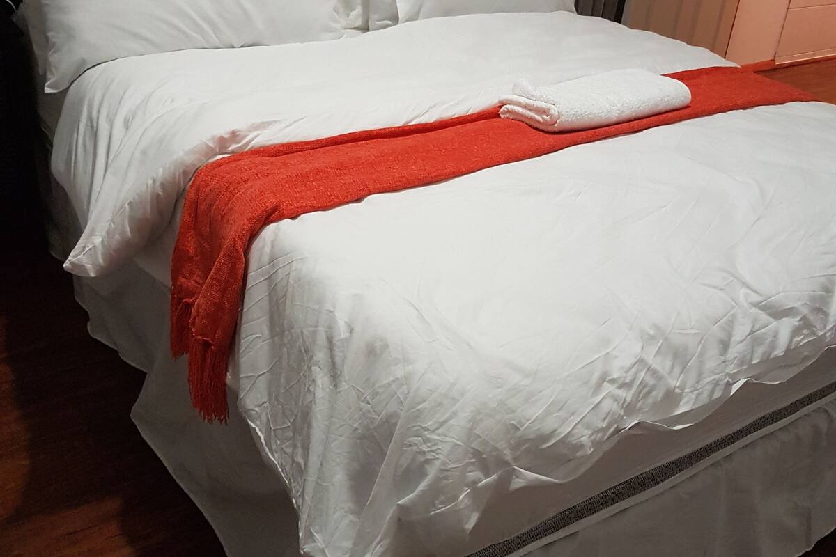 A neatly made bed with white linens and a red throw blanket, a wooden headboard, and a door to the right.