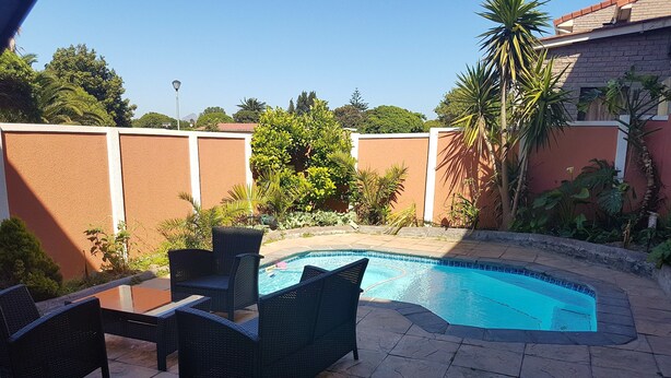 A swimming pool with a tiled edge, surrounded by a patio with wicker furniture. - Beautiful Apartment in Century City (Cape Town)