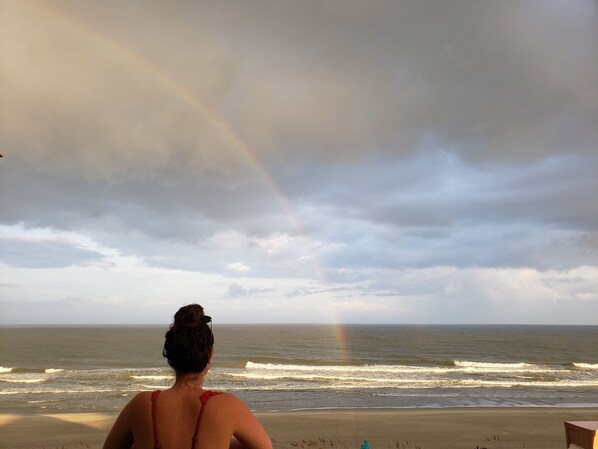 A beach scene with a person facing the ocean, a rainbow, and a cloudy sky. - Classy, Clean & Elegant Oceanfront 'Penthouse' ~ (Surfside Beach)