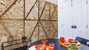 A dining area with a round table, chairs, and a variety of bowls and cups. There is a wall with a textured pattern and a door in the background. - LxWay Apartments Old Town (Lisbon)