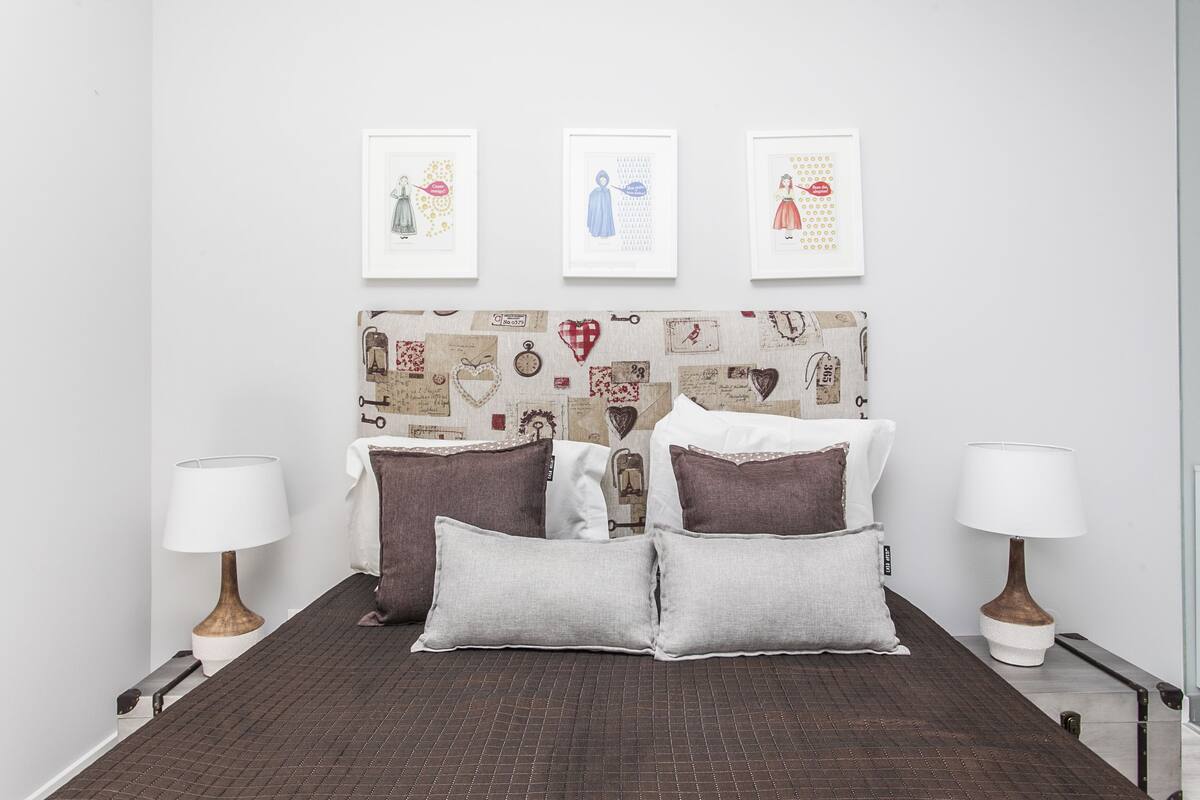 Een netjes ingerichte slaapkamer met een gestreept hoofdbord, twee nachtkastjes met lampen, en drie ingelijste kunstwerken aan de muur.