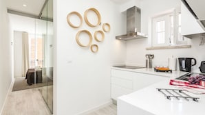 A modern kitchen with a white countertop, a stainless steel range hood, and a window with an open door. - LxWay Apartments Old Town (Lisbon)