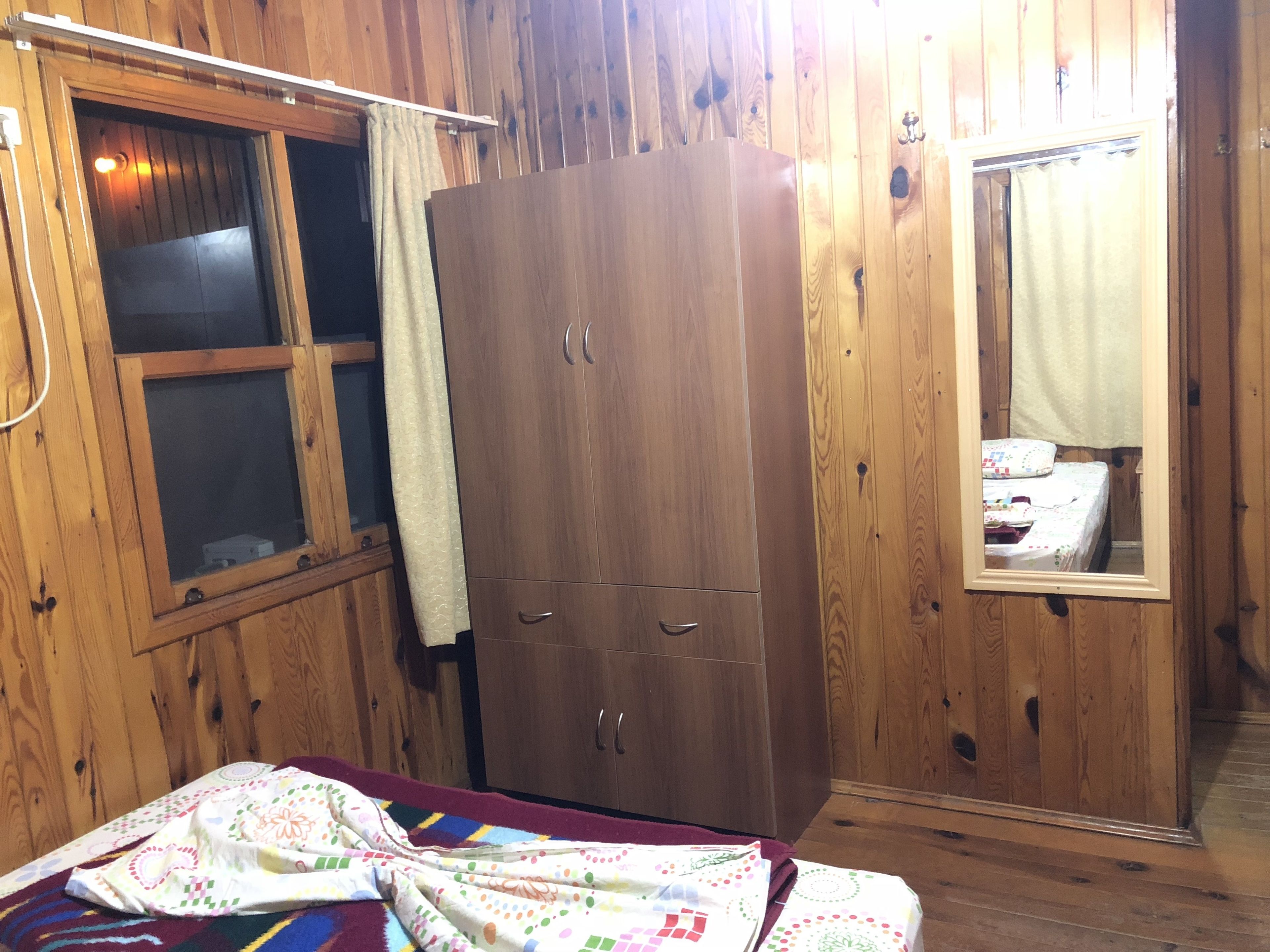 A wooden room with a bed, a wardrobe, and a window with curtains.