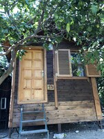 Una cabaña de madera con un portal grande, una ventana con contraventanas y una escalera que lleva a la entrada.