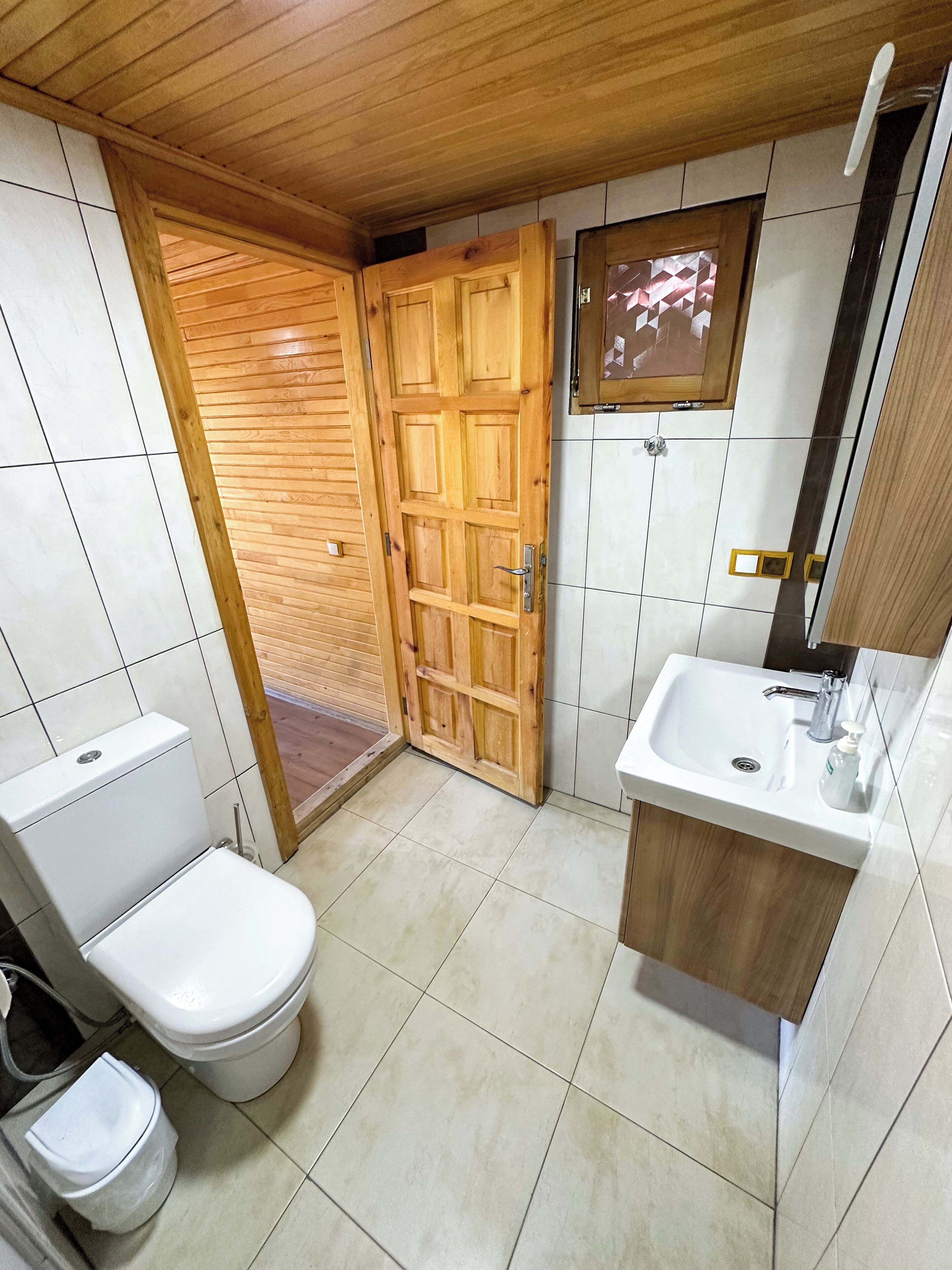 Un baño con puerta de madera, un lavabo blanco y un inodoro.