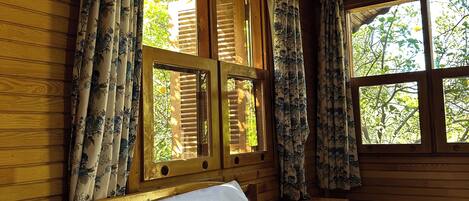 A wooden room with a bed, curtains, and windows.