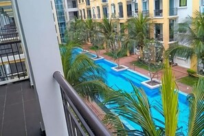 Una piscina rodeada de palmeras, un balcón con barandilla y un edificio con varios balcones.