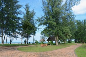 A paved pathway leading to a beach area with trees and a small structure. - Tiara Desaru Seaview Residence (Bandar Penawar)