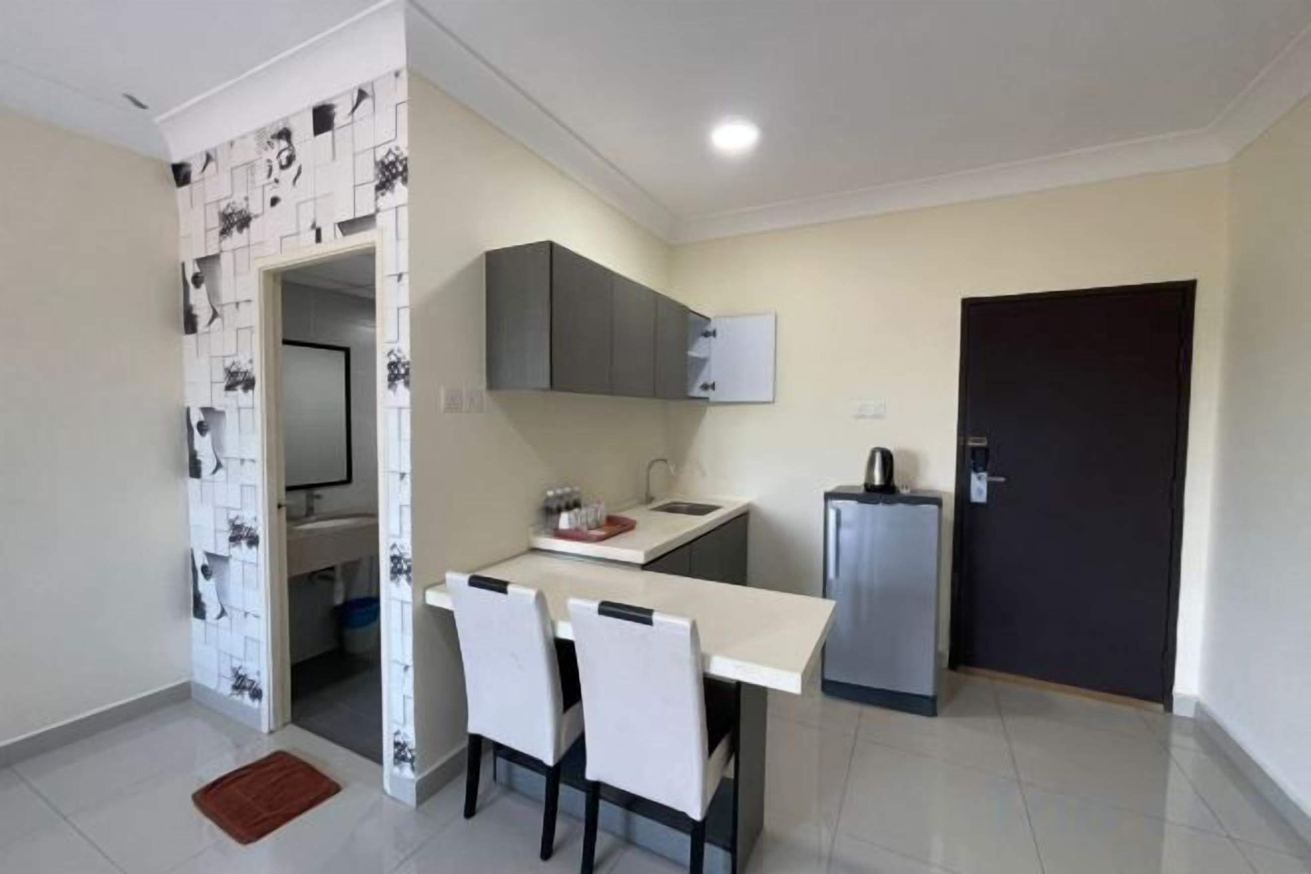 Una cocina compacta con encimera blanca, dos sillas, un refrigerador y una puerta oscura.